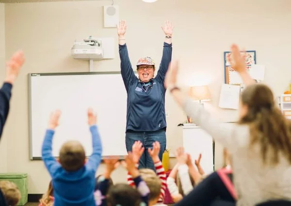 Teacher and students raising hands in classroom.